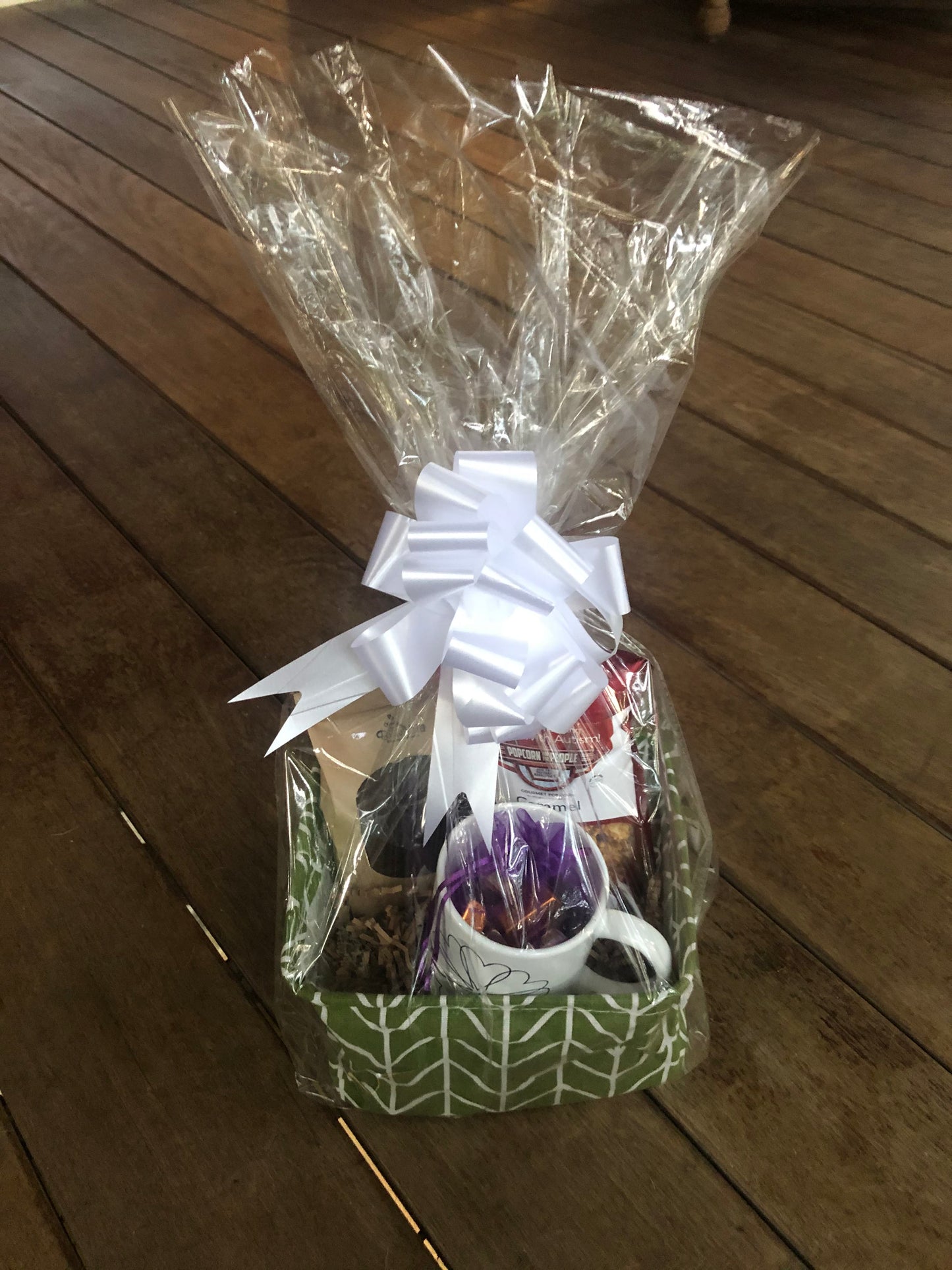 This handmade gift basket includes a choice of a ceramic mug or a stainless steel tumbler, gourmet coffee or hot cocoa mix, caramel popcorn and chocolates 