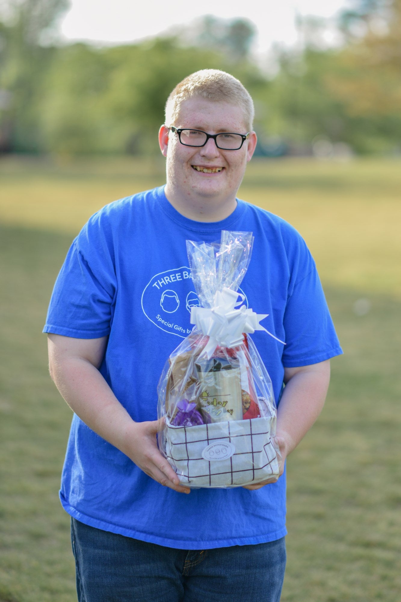 A disabled business owner with a blue shirt and glasses holding a completed "Just Because" gift basket while standing outside
