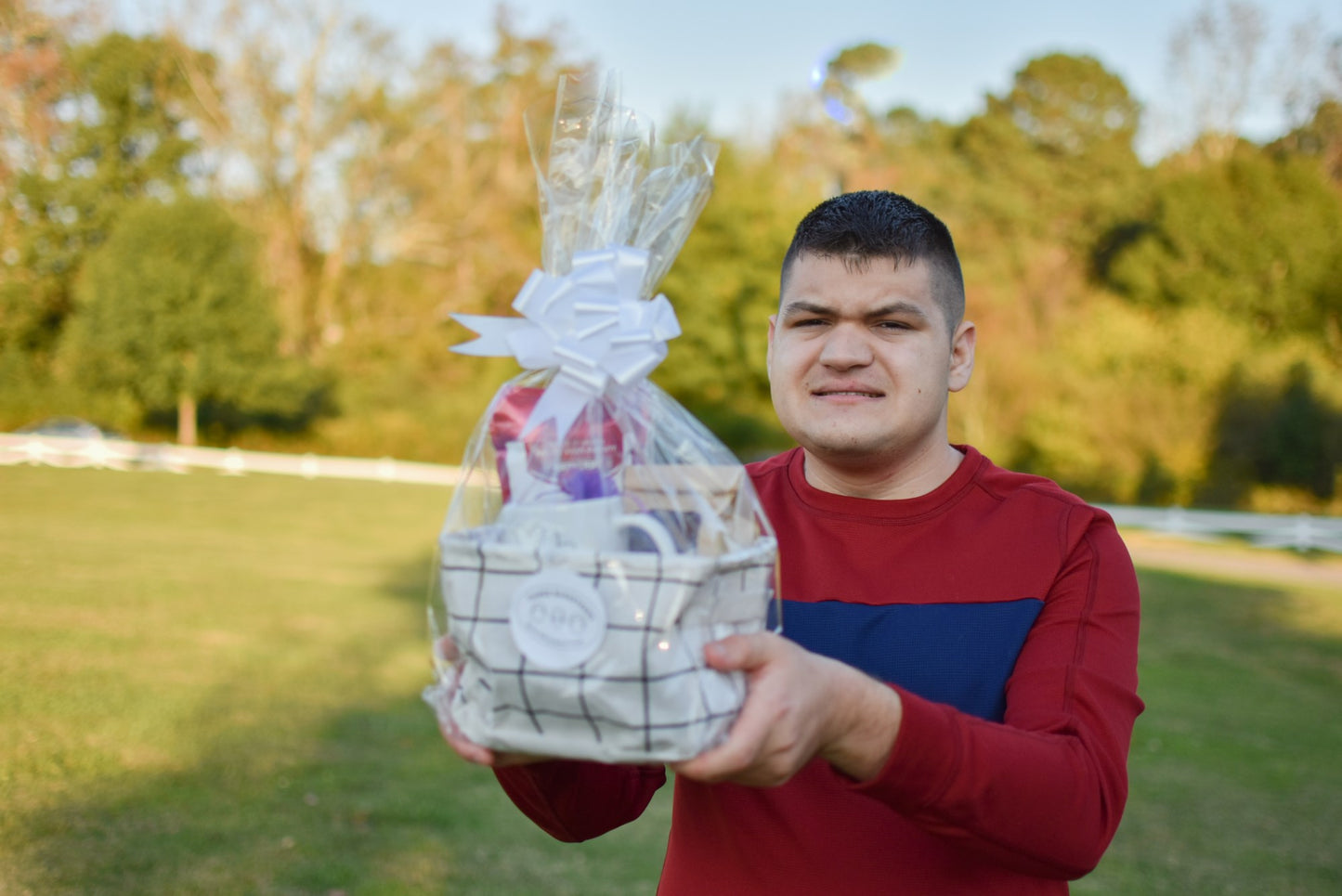 A disabled business owner with a red long sleeve shirt holding a completed "Just Because" gift basket while standing outside