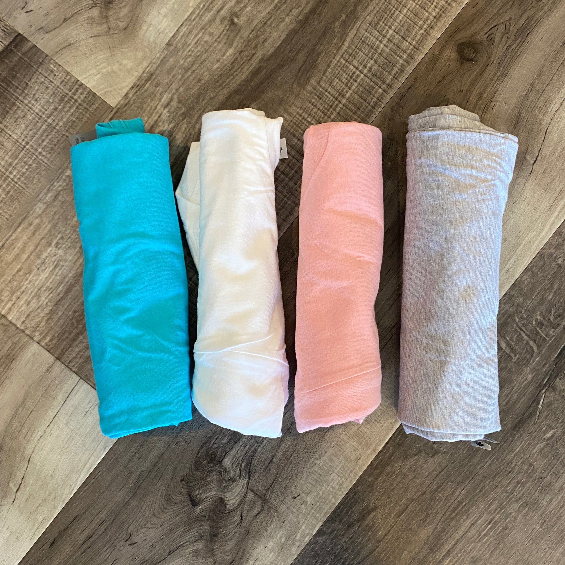 Four colors of shirts rolled up in Tahiti Blue, White, Light Pink and Heather Gray