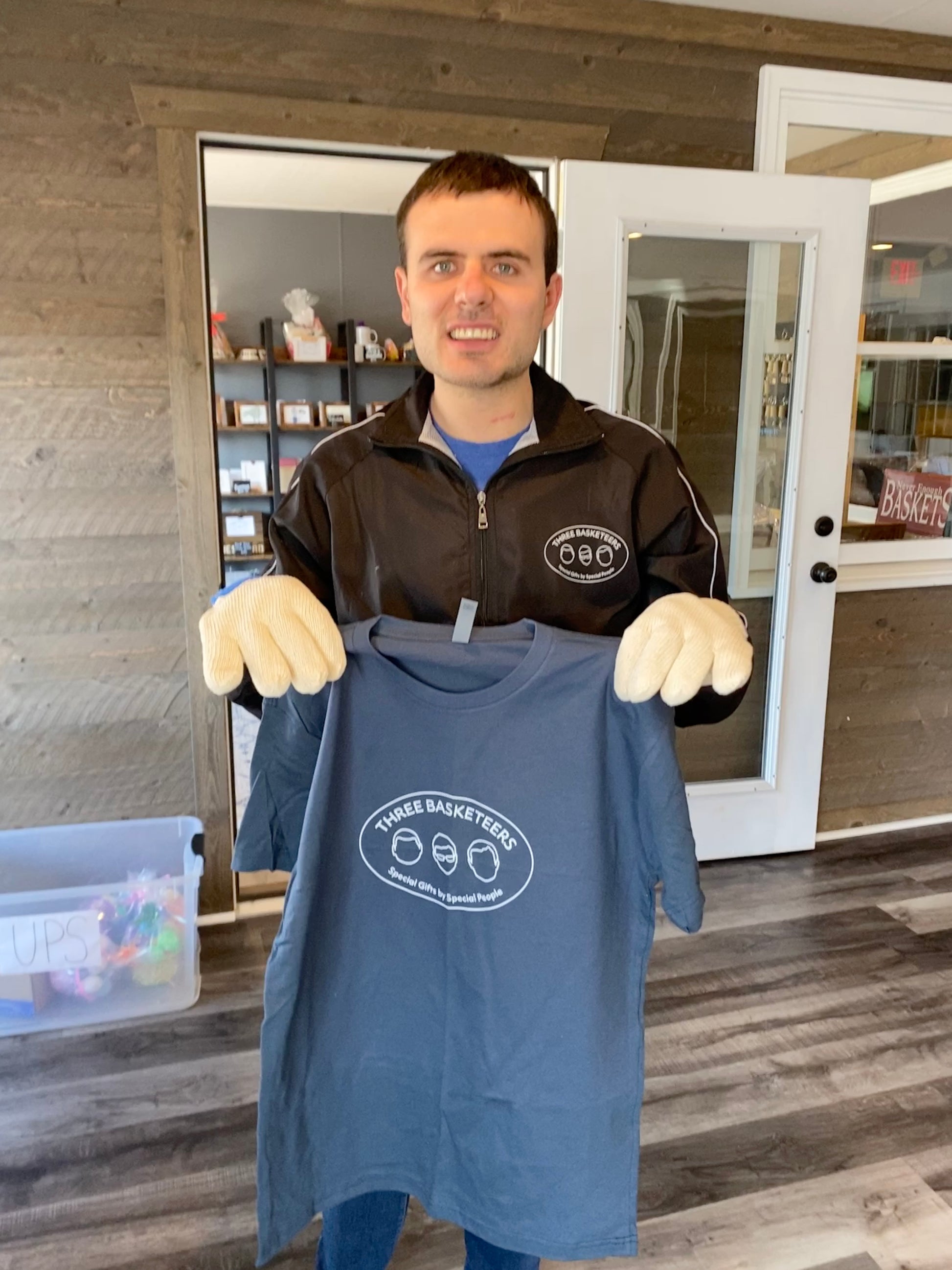 Basketeer Brett holds up a completed indigo blue t-shirt printed with the Three Basketeers logo in white