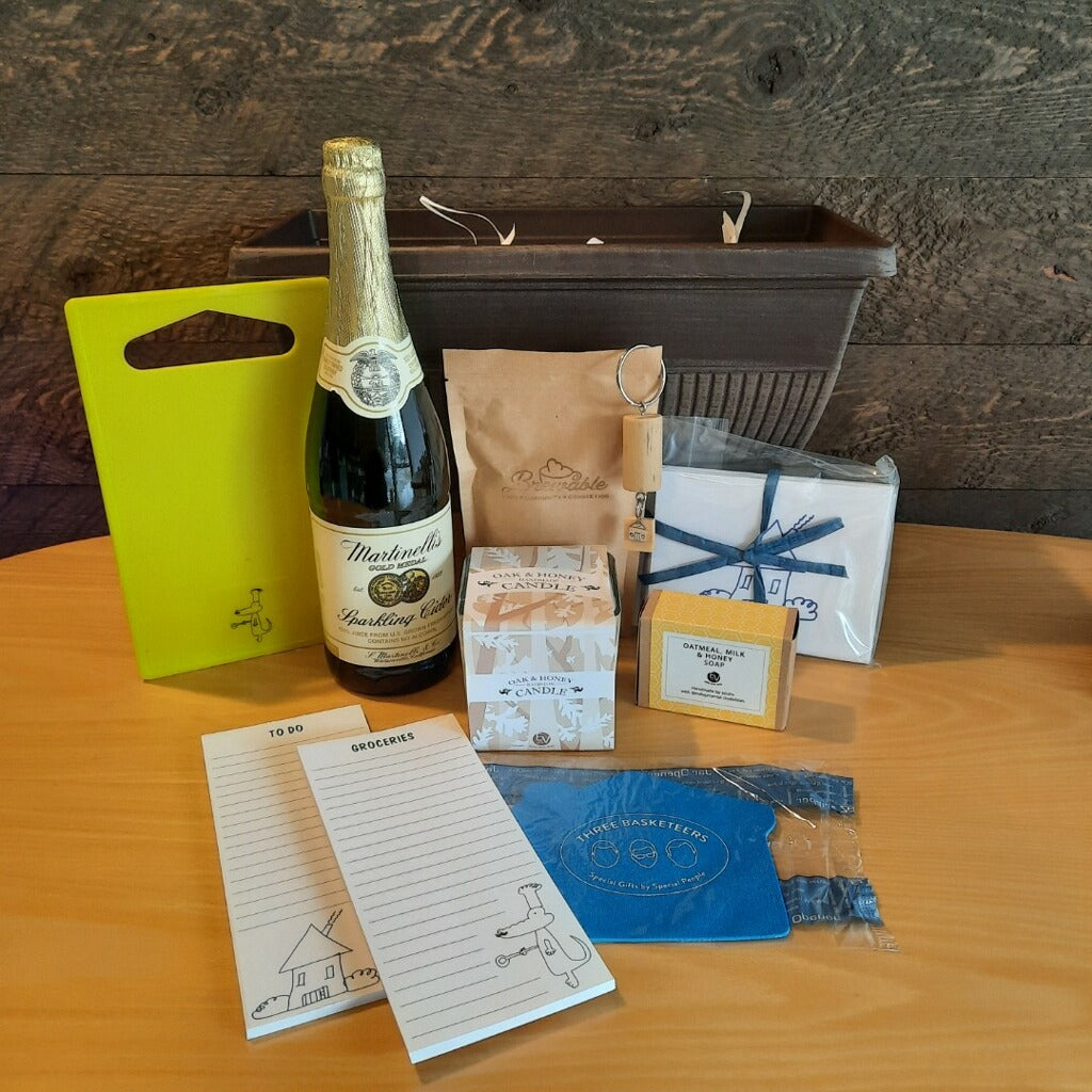 This housewarming gift basket includes gourmet coffee, sparkling juice a "Home" cork keychain, decorated cutting board, a jar opener, home themed notecards, an oak and honey double wick candle, oatmeal milk and honey scented soap bar and optional handmade coasters. 