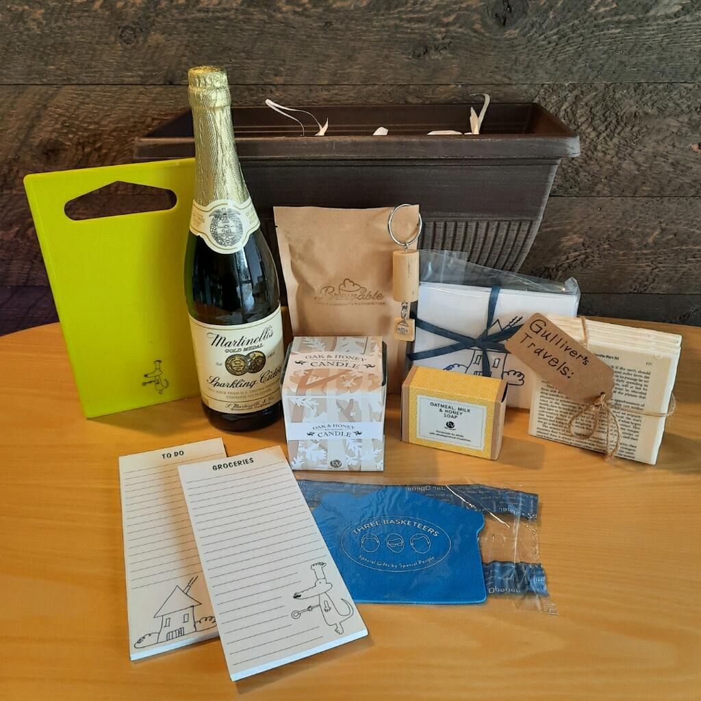 This housewarming gift basket includes gourmet coffee, sparkling juice a "Home" cork keychain, decorated cutting board, a jar opener, home themed notecards, an oak and honey double wick candle, oatmeal milk and honey scented soap bar and optional handmade coasters. 
