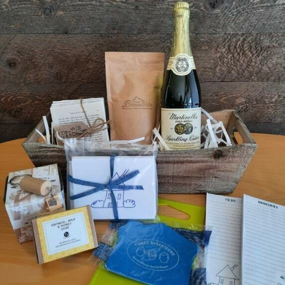 This housewarming gift basket includes gourmet coffee, sparkling juice a "Home" cork keychain, decorated cutting board, a jar opener, home themed notecards, an oak and honey double wick candle, oatmeal milk and honey scented soap bar and optional handmade coasters. 