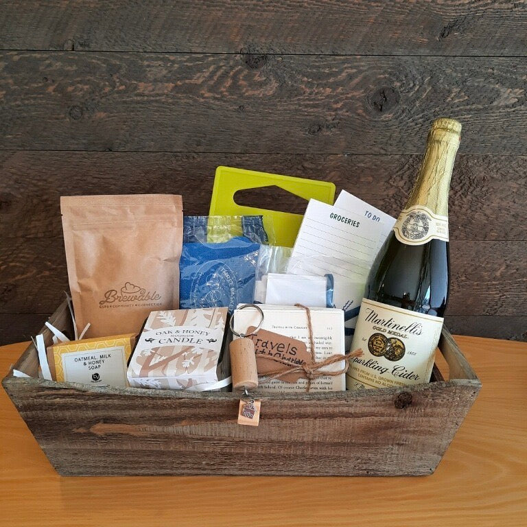 This housewarming gift basket includes gourmet coffee, sparkling juice a "Home" cork keychain, decorated cutting board, a jar opener, home themed notecards, an oak and honey double wick candle, oatmeal milk and honey scented soap bar and optional handmade coasters. 