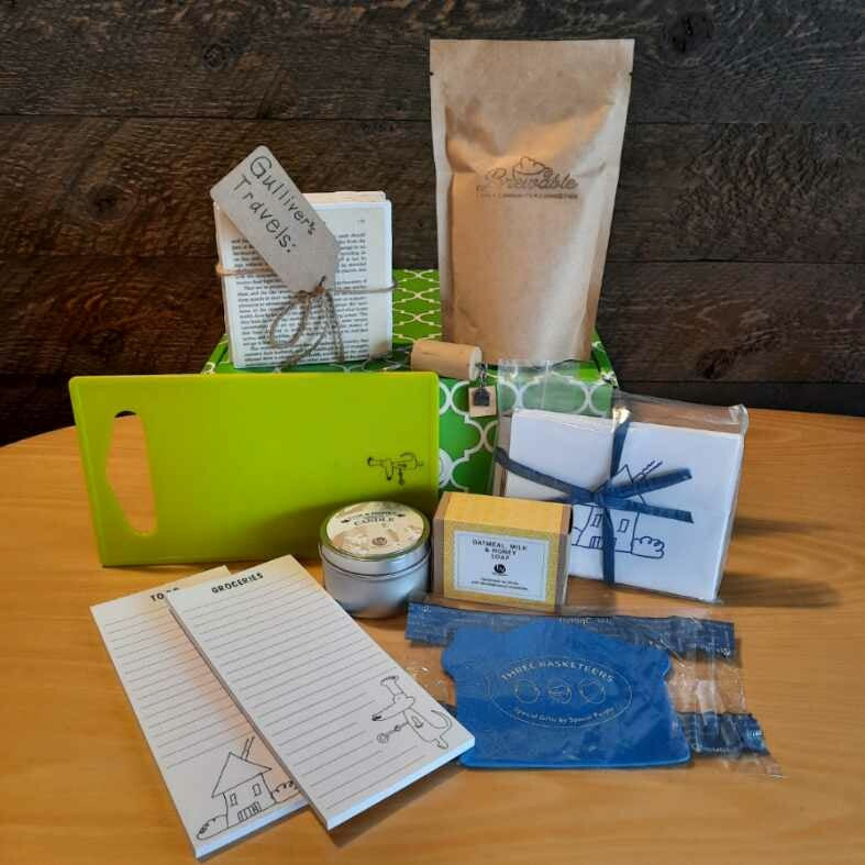 This housewarming gift basket includes gourmet coffee, sparkling juice a "Home" cork keychain, decorated cutting board, a jar opener, home themed notecards, an oak and honey double wick candle, oatmeal milk and honey scented soap bar and optional handmade coasters. 