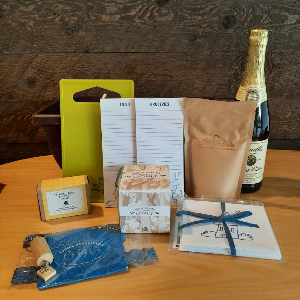 This housewarming gift basket includes gourmet coffee, sparkling juice a "Home" cork keychain, decorated cutting board, a jar opener, home themed notecards, an oak and honey double wick candle, oatmeal milk and honey scented soap bar and optional handmade coasters. 